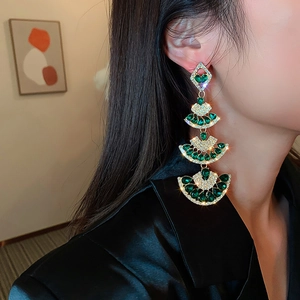 Detail view of long fan-shaped tassel earrings with green gems and gold plating