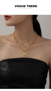 Close-up of triple-layered gold necklaces with coin pendant and OT buckle on model