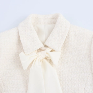 Close-up of beige tweed jacket neckline featuring a large decorative cream bow detail
