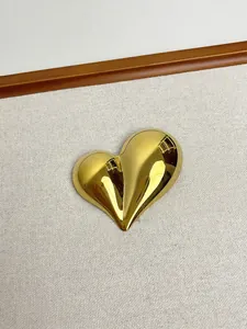 Detailed view of heart-shaped gold polished metal brooch on beige textured fabric