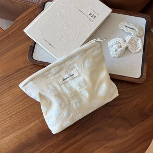 Macro view of cream textured fabric makeup bag with top zipper and simple wish label