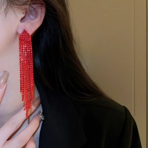 Detailed view of red tassel rhinestone earrings with long dangling chains on a model