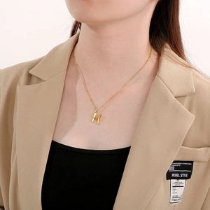 Close-up of a gold-plated H-letter pendant necklace worn with an elegant blazer