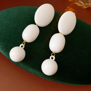 Macro detail of white geometric beaded earrings with gold rings on green velvet