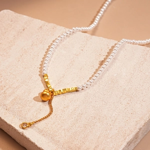 Détail du collier de perles avec pendentif cœur doré et pampille ornée de strass