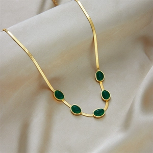 Elegant gold snake chain necklace with five green emerald-style oval stones on champagne satin