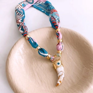 Detail of silk scarf necklace featuring golden beads and evil eye horn pendant