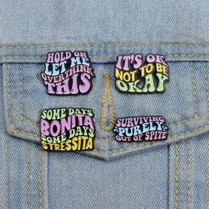 Close-up of four colorful enamel quote badges pinned on a blue denim jacket pocket