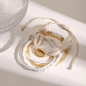 Detail of layered anklet with cowrie shells and gold beads on a sandy textured background