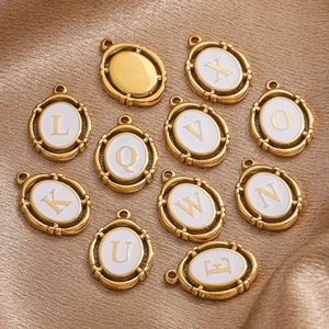 Detailed shot of golden oval A-Z letter pendants with white enamel on silk fabric