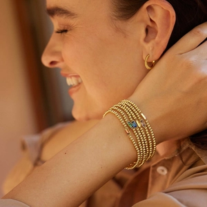 Close-up of layered gold beaded bracelets with colorful gemstone charms and hoop earrings