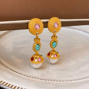 Close-up of vintage gold earrings with pink gems, teal stones, and white pearl drops