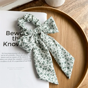 Detailed view of floral bow hair scrunchie with green daisy print on white fabric