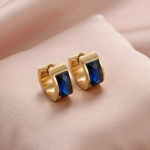 Macro shot of gold huggie hoop earrings featuring faceted rectangular dark blue gemstones