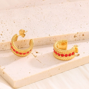Detail of vintage C-shaped gold earrings with inlaid red gemstones on stone