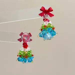 Detail of beaded Christmas tree earrings with a red bow on a transparent stand