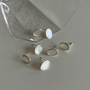 Minimalist oval white shell earrings with silver metal edges on a light gray surface