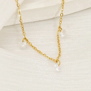 Close-up of gold chain necklace with three clear zircon stones on textured white fabric