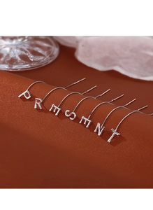 Detailed close-up of silver letter earrings spelling PRESENT on brown leather background