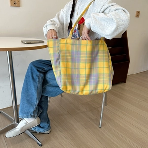 Close-up of a large plaid canvas tote bag in yellow and purple on a shoulder