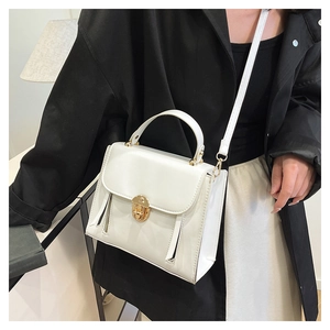 Detail of white structured handbag featuring a gold twist-lock and decorative zippers