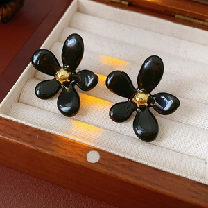 Close-up of black flower earrings with gold pistils on beige velvet jewelry box tray