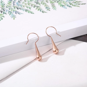 Macro detail of rose gold teardrop earrings hanging on a white geometric display