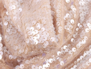 Close-up of shimmering white sequins sewn onto nude mesh fabric for a party two-piece set