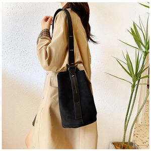 Detail showing the matte black suede texture and adjustable leather strap on bucket bag