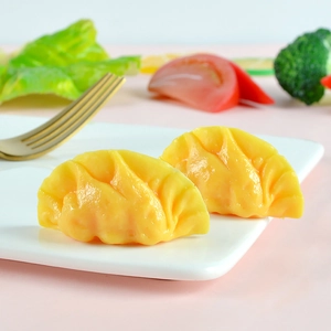 Realistic artificial dumpling models on a white plate with vegetables and a golden fork