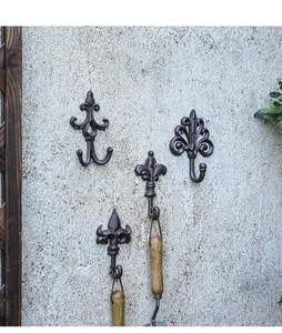 Detail of vintage fleur-de-lis cast iron hooks mounted on a rustic concrete wall