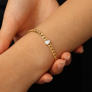 Gros plan d'un bracelet gourmette doré orné d'un zircon scintillant en forme de poire