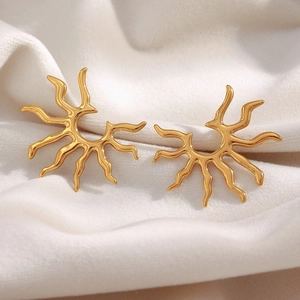 Detail of gold sunburst stud earrings on soft pleated fabric with metallic luster