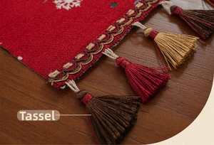 Detail of festive red Christmas table runner featuring white snowflakes and woven tassels