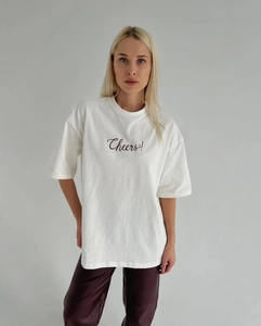 Vue détaillée de l'imprimé 'Cheers!' sur un t-shirt blanc à col rond et manches courtes