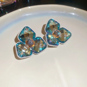 Close-up of teal diamond-set floral stud earrings on a minimalist white tray