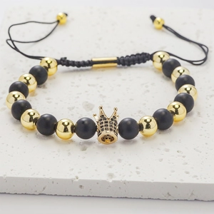 Detail of beaded bracelet with black matte beads and gold crown charm on stone slab