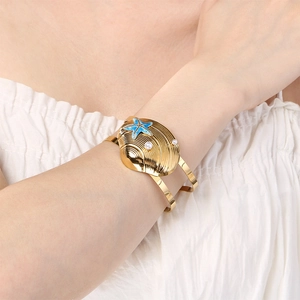 Detailed shot of ocean-themed gold cuff with sea shell, blue starfish, and white pearl