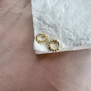 Nahaufnahme goldener Perlen-Ohrringe auf Seide und strukturiertem Steinhintergrund