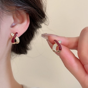 Detail of red enamel and diamond ribbon earrings shown in hand and on the ear