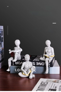 Dettaglio di tre sculture di lettori in resina bianca con trama di giornale su una scrivania
