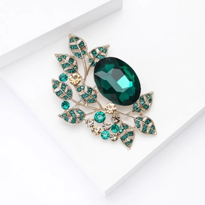 Macro shot of gold leaf brooch with emerald gemstone and sparkling champagne rhinestones
