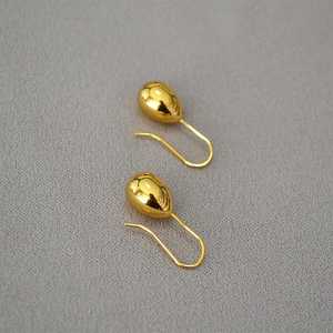 Macro shot of polished gold-plated teardrop earrings on a grey textured fabric background