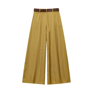 Dettaglio macro dei pantaloni larghi giallo senape con riflessi metallici e cintura marrone