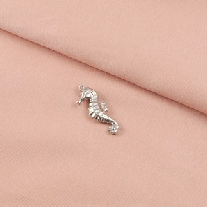Macro detail of a silver stainless steel seahorse pendant on a soft pink fabric surface