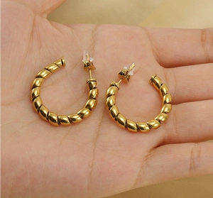 Close-up of gold twisted C-shaped earrings held against a soft fabric background