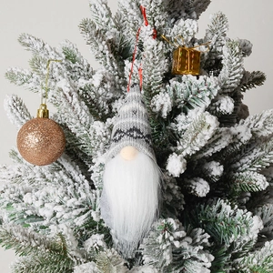 Close-up of a knitted grey gnome ornament hanging on a snowy Christmas tree branch
