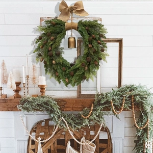 Rustic Christmas wreath with pine needles, burlap bow and bell hanging on fireplace mantel