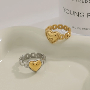 Detailed view of hollow chain band heart rings in gold and silver on a ceramic tray