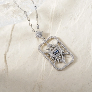 Macro shot of silver evil eye pendant with blue and white zircons on beige sand texture